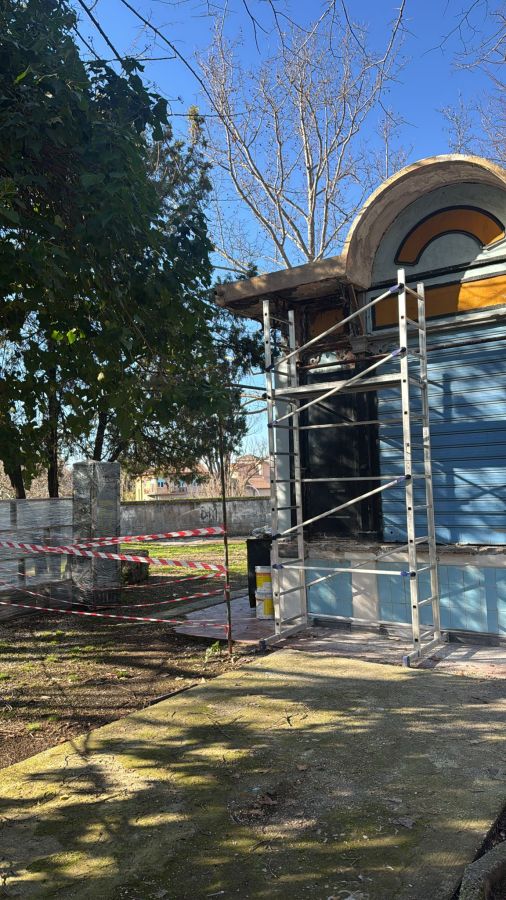 A partially constructed building with scaffolding, surrounded by trees and caution tape, under a clear blue sky.