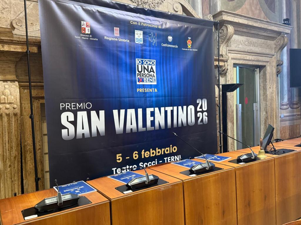 A stage setup for the San Valentino 2026 award ceremony, featuring a large banner with the event title and details about the location and dates, alongside microphones and tables for speakers.