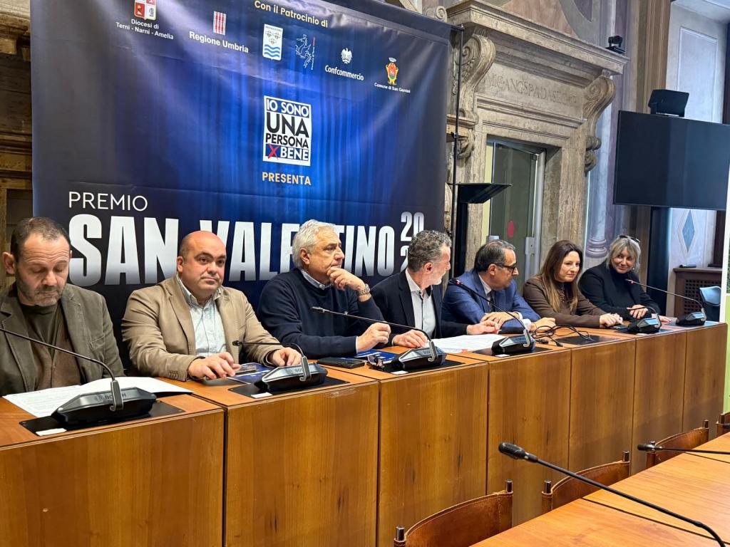 A panel of speakers seated at a table during the presentation of the Premio San Valentino, featuring a backdrop with the event's branding and logos from various organizations.