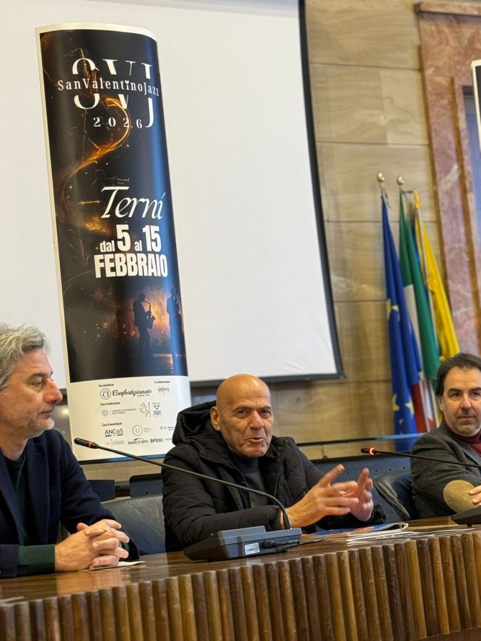 Three men seated at a table during a press conference, discussing the San Valentino Jazz festival in Terni, Italy. A promotional banner for the festival is visible in the background.