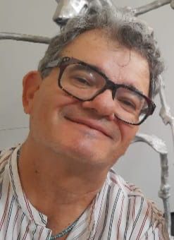 A smiling middle-aged man with glasses, wearing a striped shirt, posing in a bright environment.