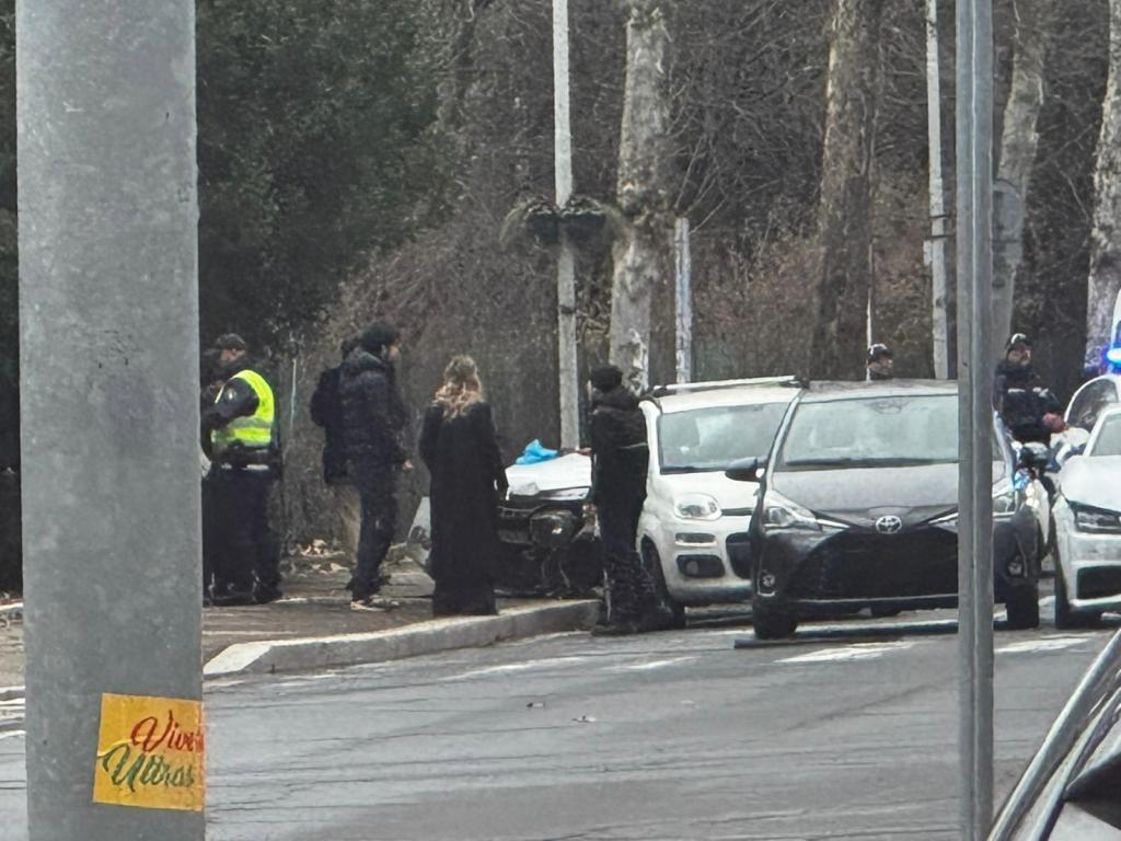 A scene showing a small group of people, including individuals in police uniforms, gathered near parked cars in a street setting, with trees in the background. A sign visible on a pole reads 'Vivir Ultras'.
