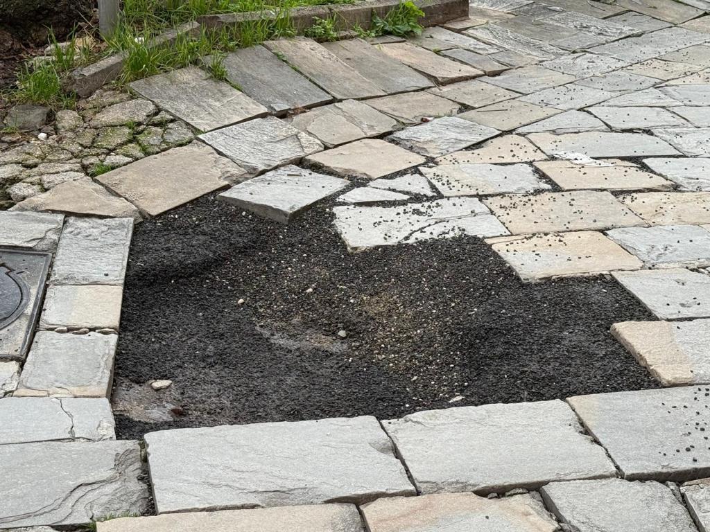 A section of cobblestone pavement with a partially filled hole, revealing dark gravel and soil underneath.