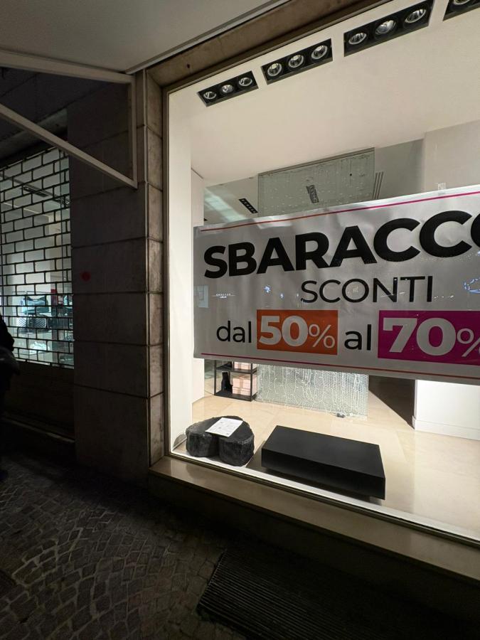 Storefront with a large sale sign reading 'SBARACCO SCONTI' offering discounts from 50% to 70%, featuring display items visible through the window.