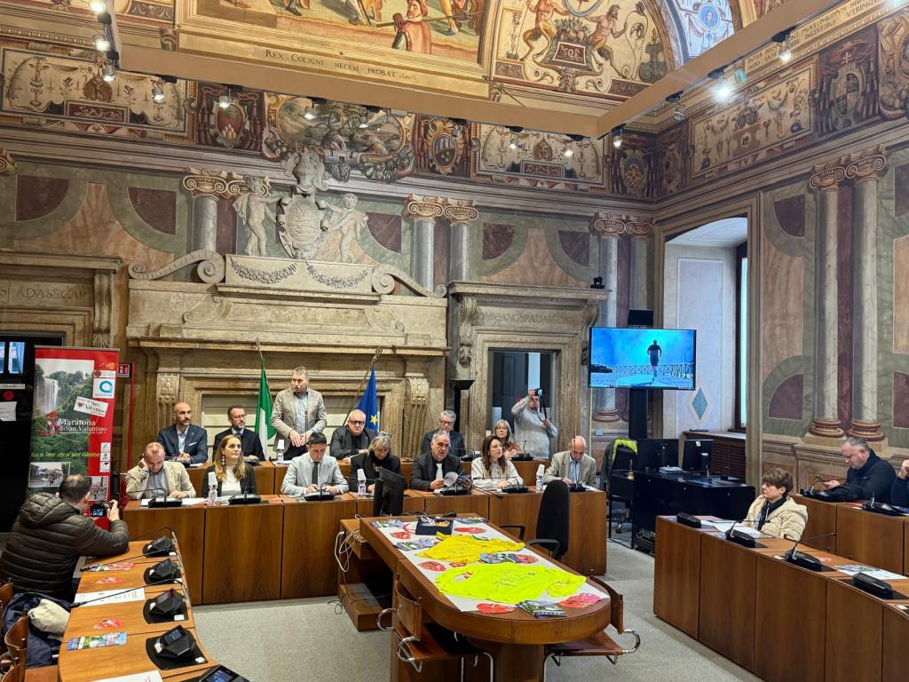 A formal meeting taking place in a historically decorated room with people seated around a table, featuring presentations and technology displays.