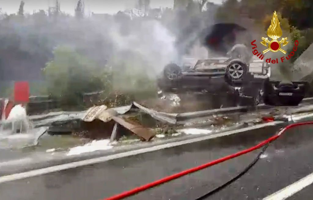A flipped vehicle on the side of a road, surrounded by smoke and debris, with emergency response equipment visible.