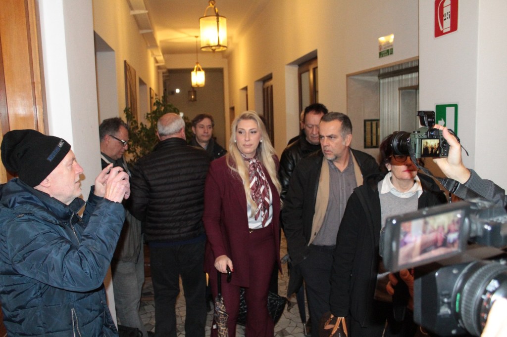 A group of people gathered in a hallway, with one individual in the foreground taking a photograph, while another person leads others down the corridor.