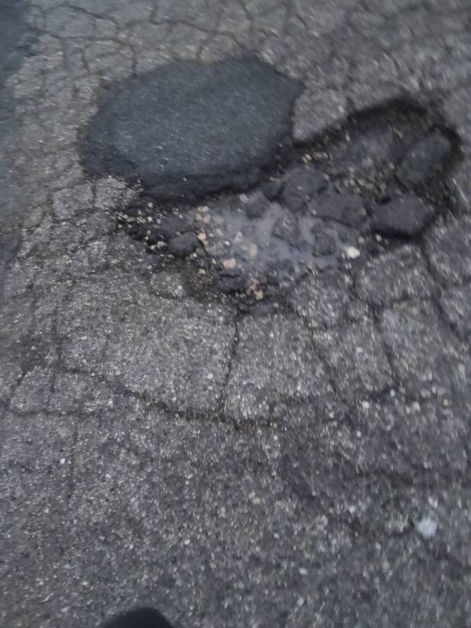 Close-up of a damaged asphalt pavement showing large cracks and potholes.