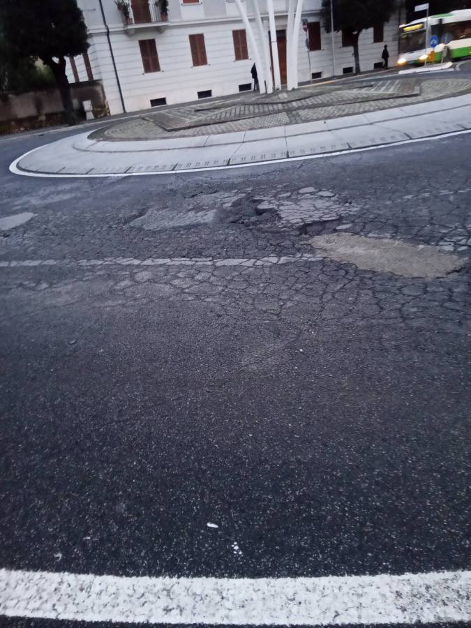 A cracked and uneven road surface at a circular intersection, with a nearby building in the background.