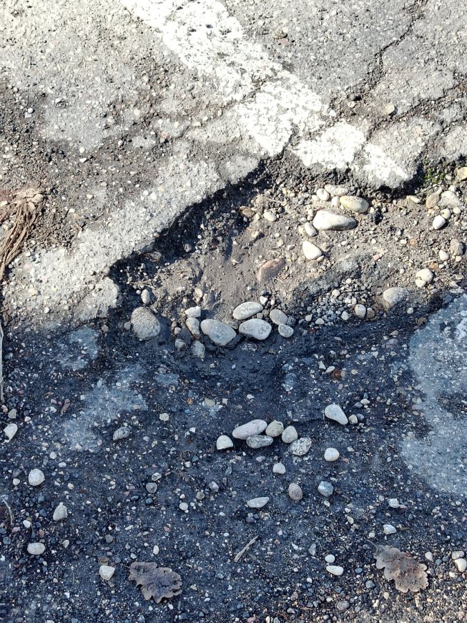 A close-up view of a pothole in a gravel road filled with small stones and dirt.