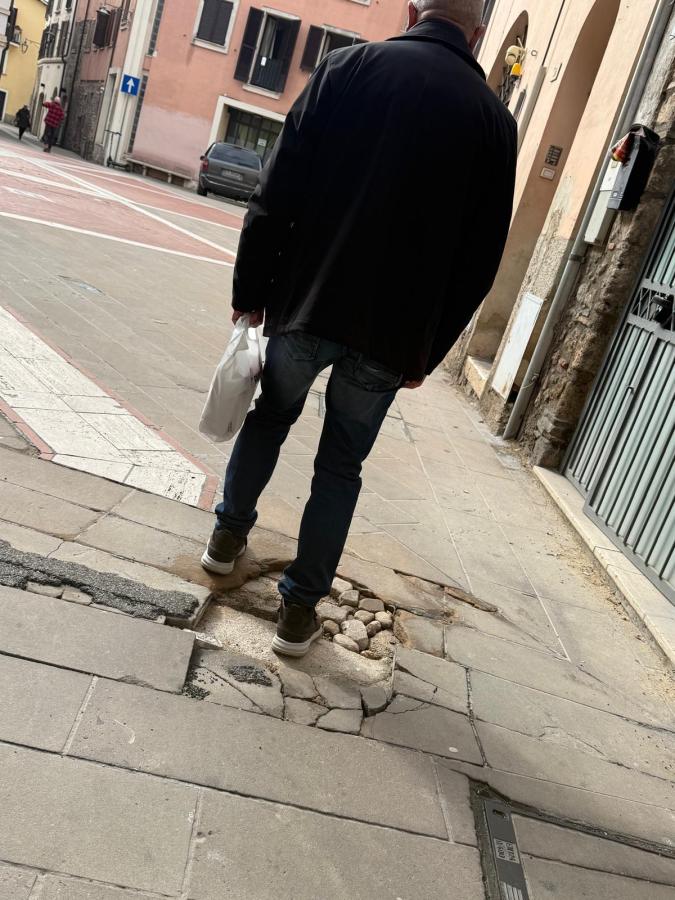 A man walking down a cobblestone street with a bag in his hand, showing uneven pavement and a rustic urban setting.