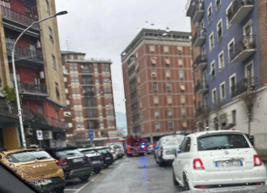 A street scene showing parked cars and apartment buildings, with a hazy view through a rain-covered window.
