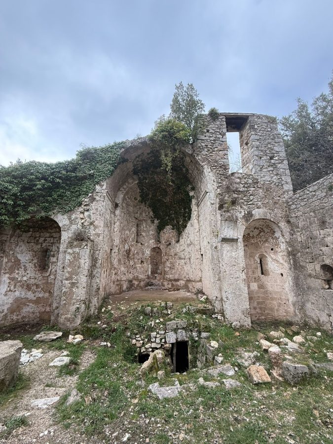 Ruins of an old stone structure overgrown with vegetation, featuring archways and a grassy area in the foreground.