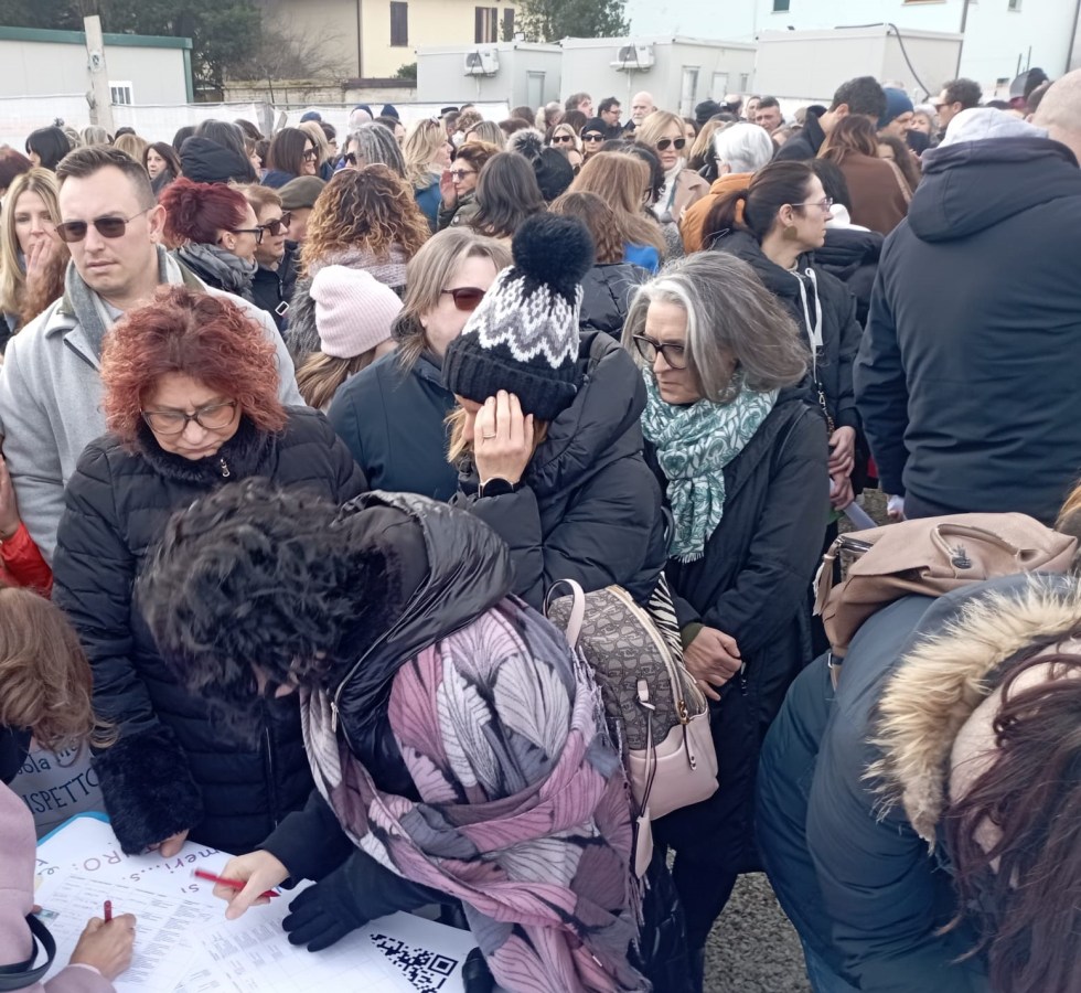 A large crowd of people standing close together, some with sunglasses and winter attire, gathered around a table where individuals are signing a document.