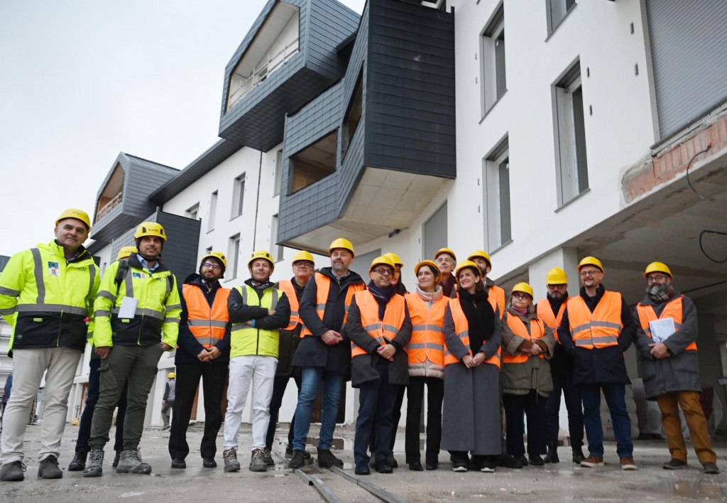 Group of construction professionals wearing safety vests and hard hats at a building site.