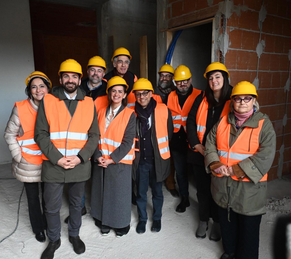A group of ten individuals wearing hard hats and reflective vests posing together inside a construction site.