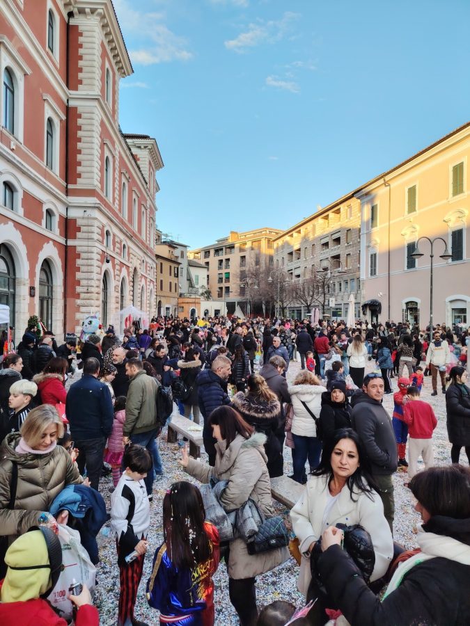 A busy plaza filled with large crowds of people, some in costumes, enjoying a festive atmosphere under a clear blue sky.