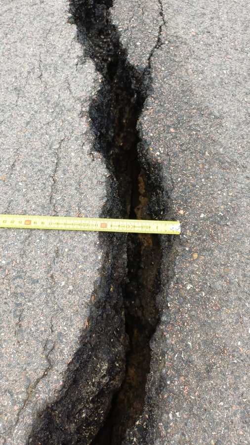 Close-up of a road crack with a measuring tape showing its width.