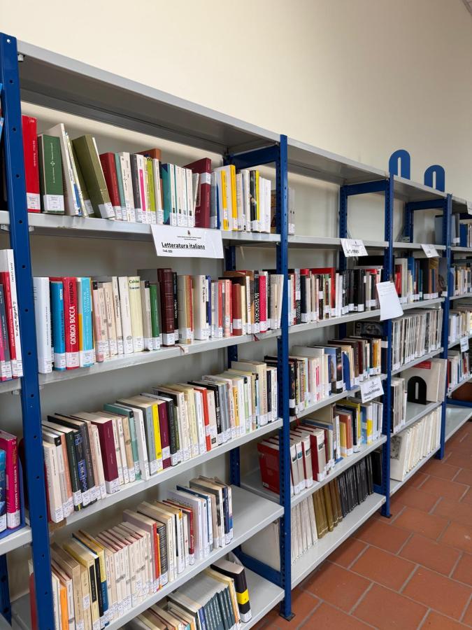 A row of bookshelves filled with various books, labeled in Italian, in a library setting.