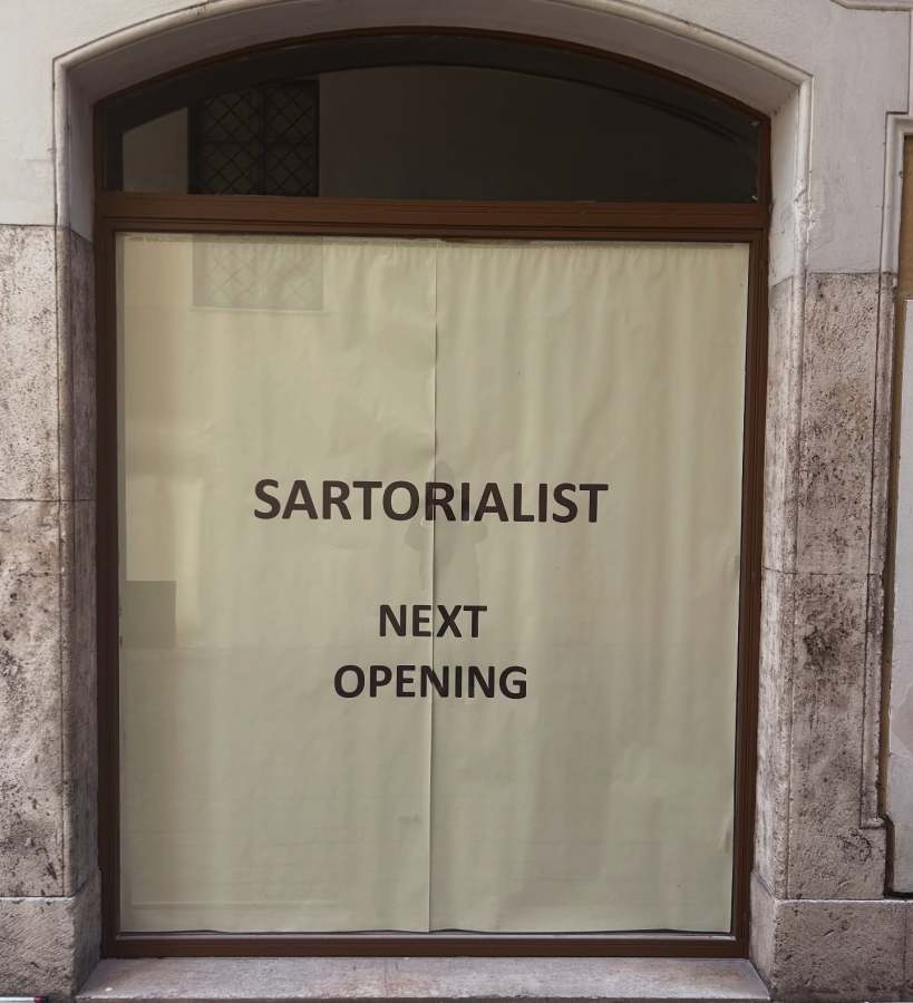 A storefront with a beige paper covering displaying the words 'SARTORIALIST' and 'NEXT OPENING' in bold black letters.