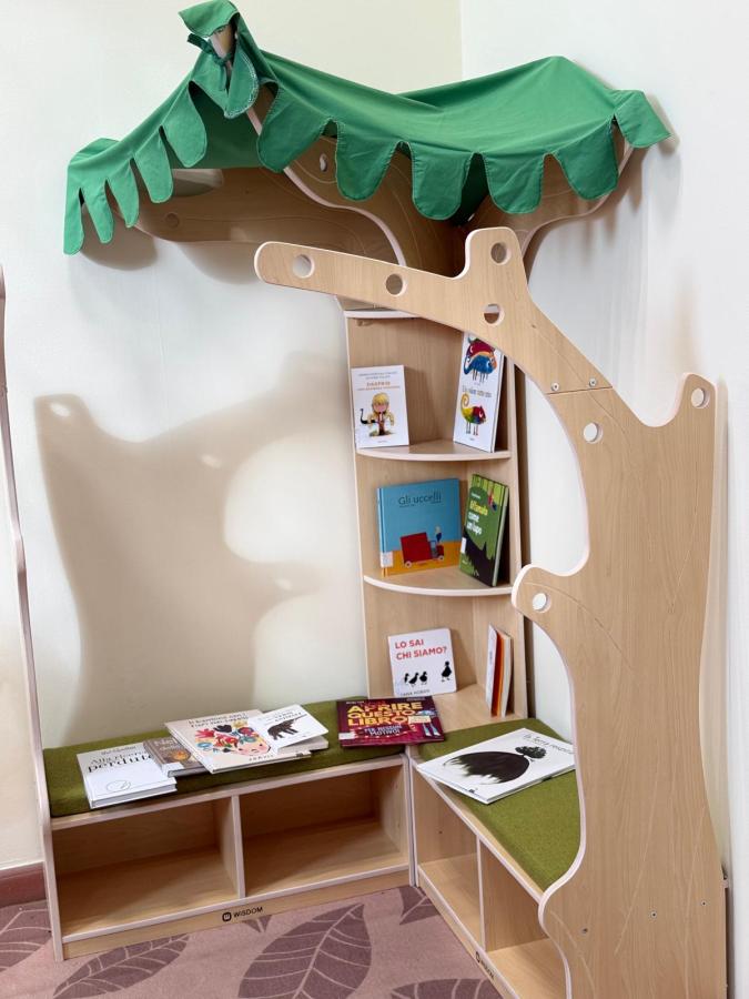 A wooden bookshelf designed as a tree with a green canopy, featuring shelves filled with children's books and a cozy reading nook.