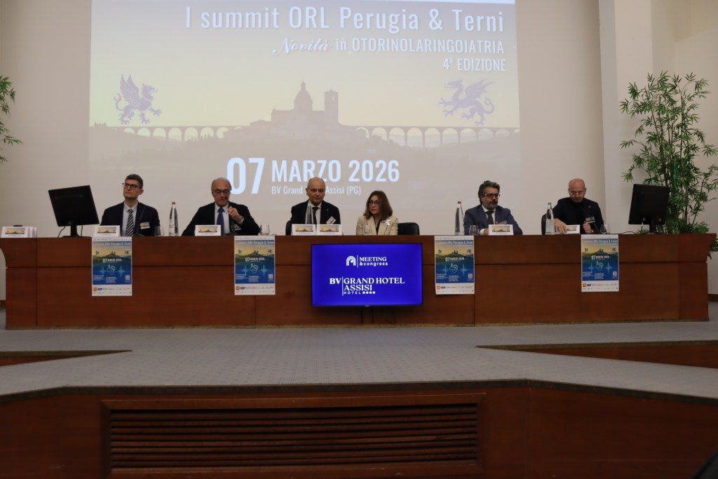 A panel of speakers at a conference table during the I summit ORL Perugia & Terni event, with a presentation background displaying the event details and a banner advertising the summit.