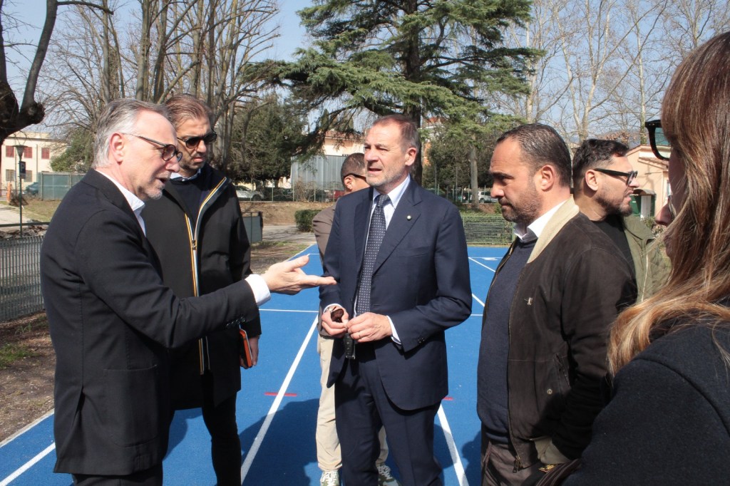 Group of professionals discussing on a blue athletic track in an outdoor setting, with trees in the background.