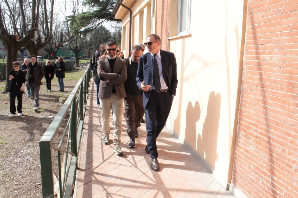 A group of people walking along a pathway next to a building, with some trees in the background.