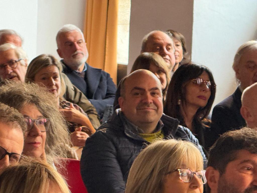 A diverse audience of people sitting in a conference or seminar setting, with some attendees smiling and others appearing engaged.