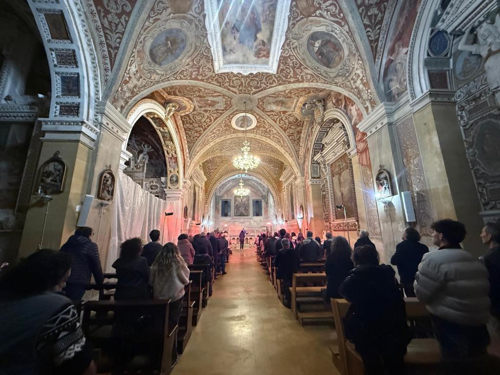 Interior view of a beautifully decorated church filled with worshippers attending a service, featuring ornate frescoes and a chandelier.