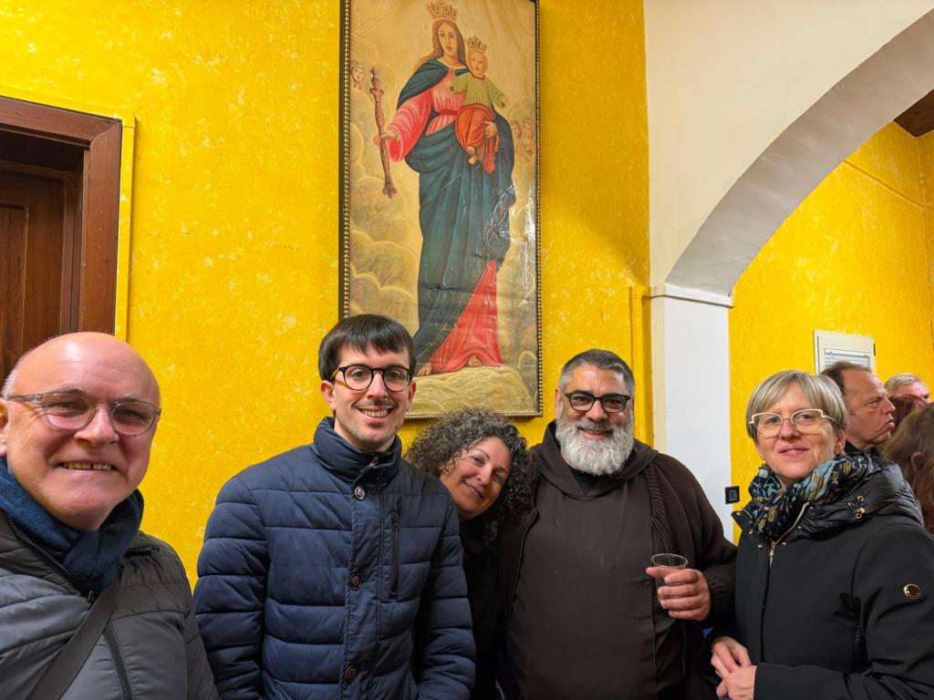A group of five smiling individuals posing for a photo in front of a religious painting, with a bright yellow wall in the background.