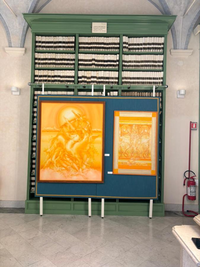 An indoor space featuring a large bookshelf filled with files, alongside two vibrant orange artworks displayed on a blue backdrop.