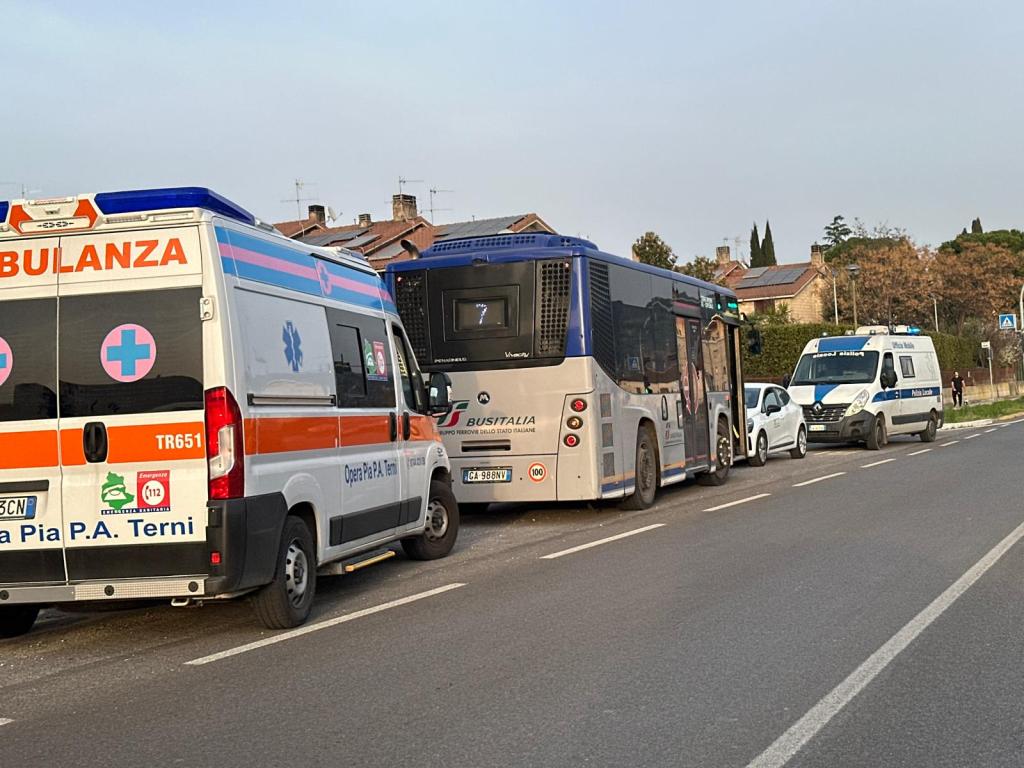 An ambulance and police vehicle parked on the roadside with a bus stopped in front, in a residential area.