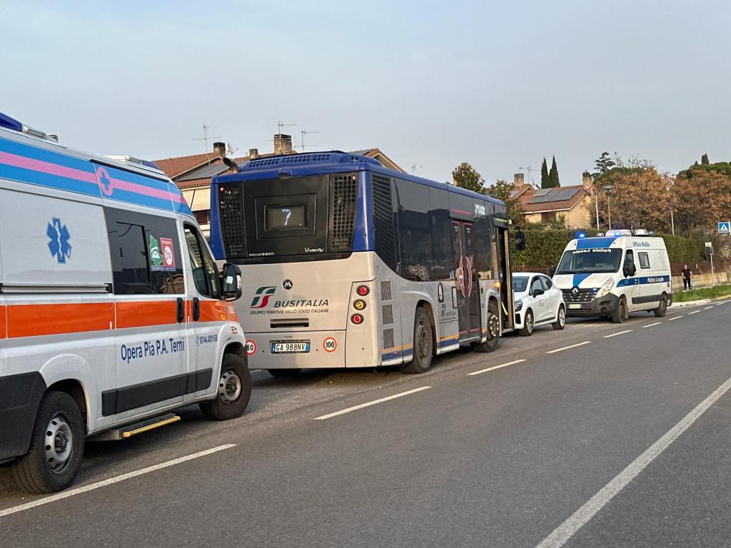 A view of a road featuring an ambulance, a public bus labeled 'BusItalia', and another emergency vehicle with flashing lights, parked alongside the roadway.