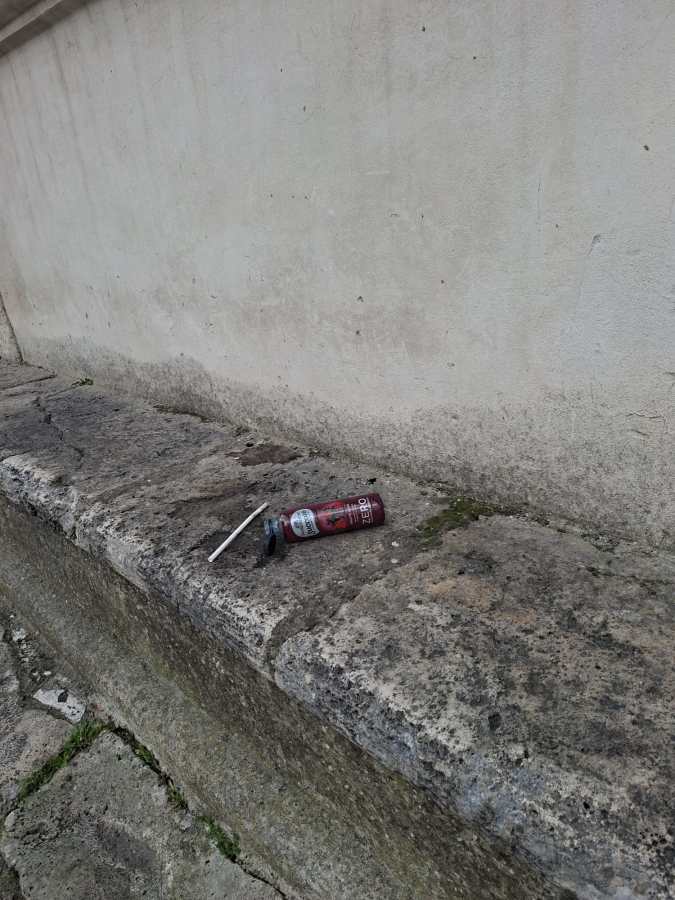A discarded can and straw resting on a stone surface next to a wall.