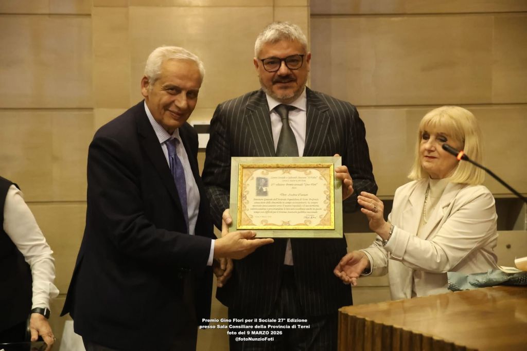 A group of three people at an award ceremony, one holding a framed certificate while the others present look on with smiles.