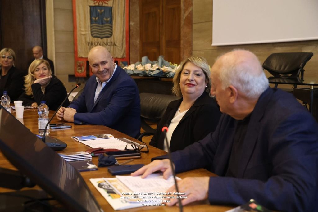 A meeting in a conference room with several participants including a smiling man and a woman, engaged in conversation at a long wooden table.