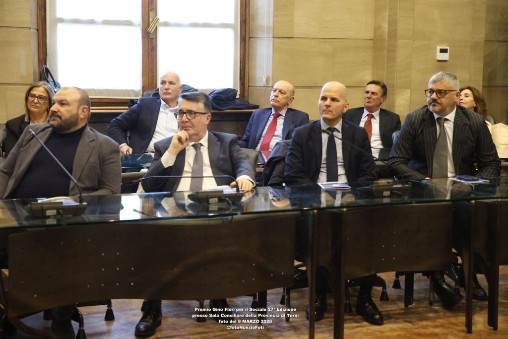 A group of individuals seated around a conference table in a meeting room, with a focus on several men in business attire, attending an event.
