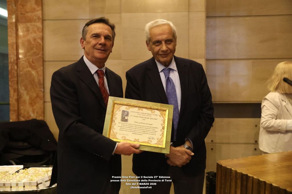 Two men in business attire, one presenting a certificate of recognition to the other in a formal setting.