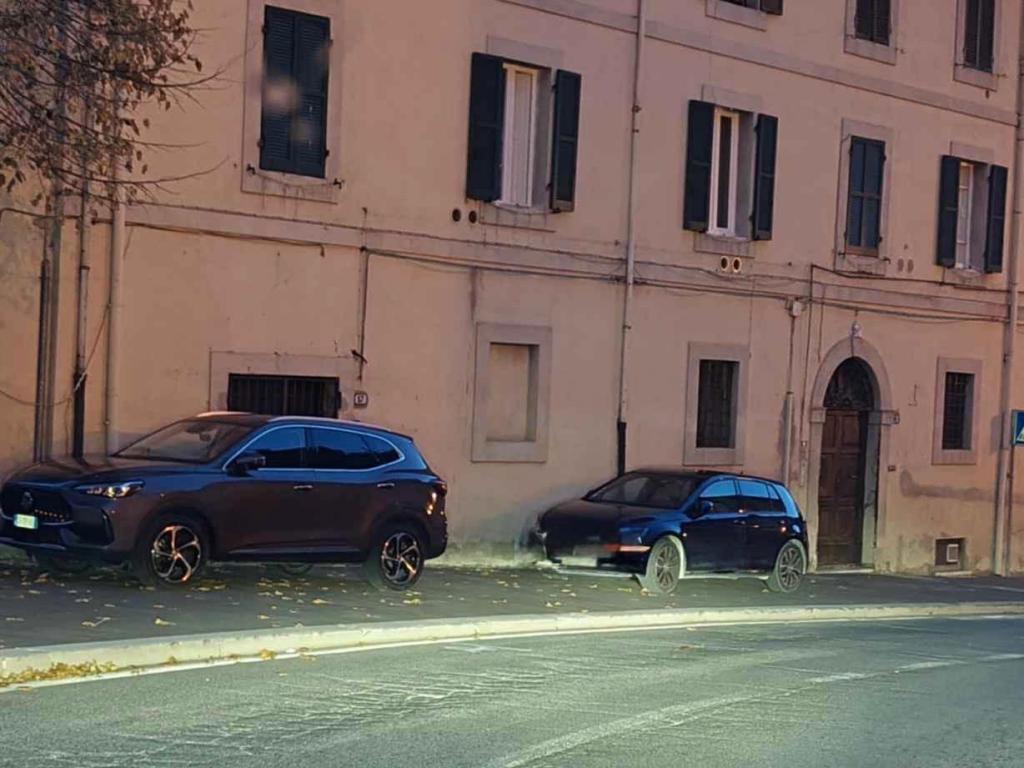 Two parked cars on a street beside a building with shuttered windows and a door.