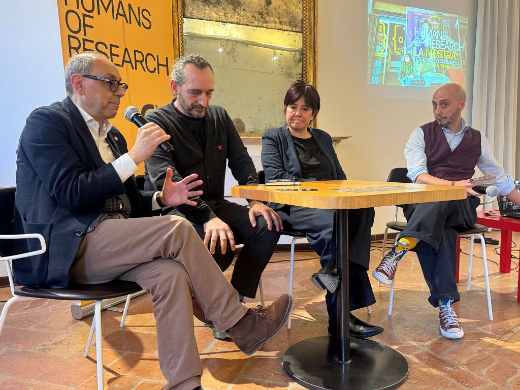 Four speakers engaged in a discussion at a panel event, sitting around a wooden table with a 'Humans of Research' banner in the background.