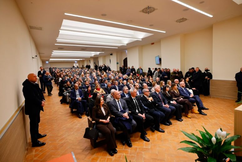 A large audience seated in a formal setting, with attendees dressed in business attire, gathered for an event in a well-lit room.