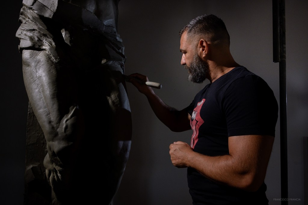 A sculptor meticulously working on a statue, holding a tool while focusing on the details of the sculpture.